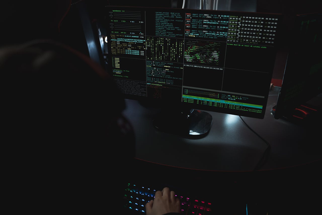 Dark room setup with code displayed on PC monitors highlighting cybersecurity themes.
